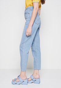 Jeans de tiro alto en azul claro con bolsillos laterales y pierna estrechada, combinados con sandalias de plataforma gruesa en azul claro.