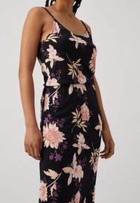 Robe à motifs floraux en tissu noir avec des fleurs roses et violettes. Elle présente des bretelles fines et une taille cintrée pour une silhouette harmonieuse.