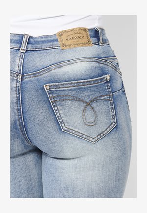 Világoskék farmernadrág márkázott világosbarna bőrfolttal, díszöltéssel a hátsó zsebben és fitted fazonnal.