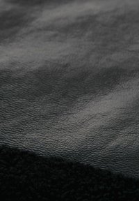 Černá texturovaná kůže a měkká černá látka se setkávají, ukazují hladký, lesklý povrch a huňatý okraj s kontrastními texturami.