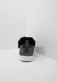 Jednoduchý černý sportovní sneaker s bílou podrážkou a černým chlupatým podšívkou, zobrazený zezadu na pozadí jednoduchého bílého rohu.