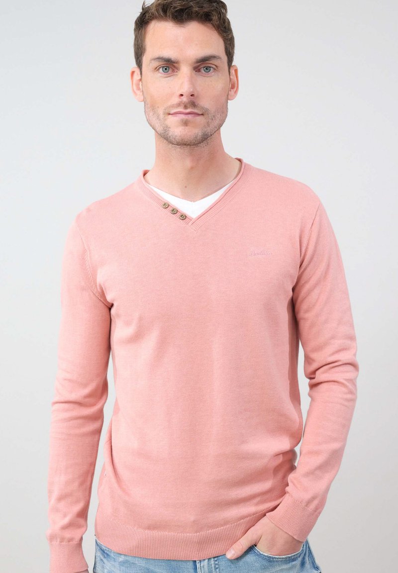 Pull en V rose clair à manches longues, avec trois boutons décoratifs au niveau du col et un ourlet côtelé.