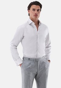 Weißes Hemd mit subtiler Struktur, Button-Down-Kragen und langen Ärmeln, kombiniert mit grauen, gefalteten Hosen.