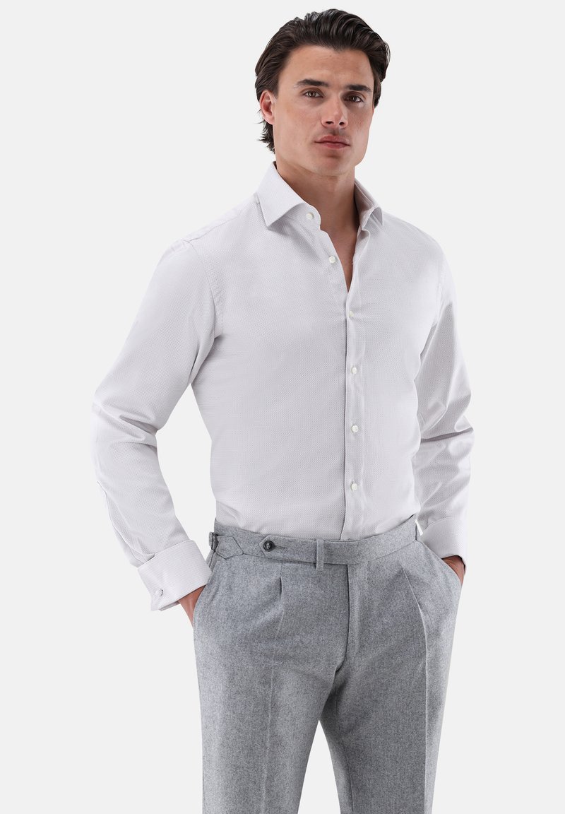 Weißes Hemd mit subtiler Struktur, Button-Down-Kragen und langen Ärmeln, kombiniert mit grauen, gefalteten Hosen.