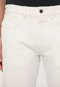 Jeans de mezclilla blanca con una cintura de media altura, diseño clásico de cinco bolsillos, herrajes de metal y un sutil detalle de costura.