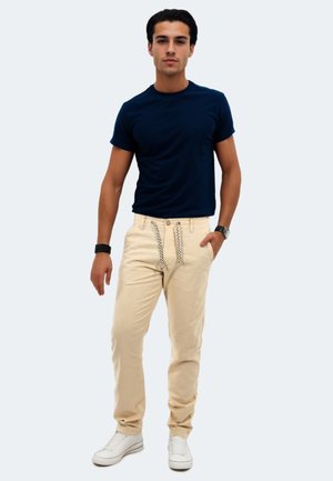Marineblaues Kurzarm-T-Shirt und beiges Hose mit Kordelzug und gemusterten Akzenten, kombiniert mit weißen Sneakers. Einfaches, lässiges Outfit.