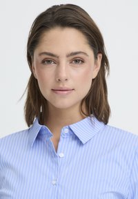 Világoskék ing függőleges fehér csíkokkal, klasszikus gallérral, gombos elejével és sima szövettextúrával.