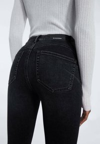 Černé džíny z denimu s vysokým pasem, které mají dvě zadní kapsy, jemné oprání a šedé stehy. V kombinaci se světle šedým ribbovaným topem.