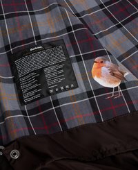 Wewnętrzna część kurtki Barbour z szaro-czarną kraciastą strukturą, pomarańczowymi i czerwonymi akcentami, z ilustracją ptaka oraz metką pielęgnacyjną.