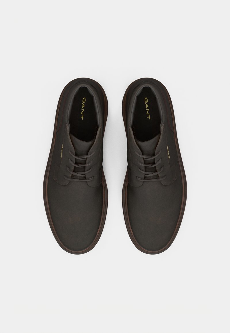 Chaussures en cuir marron foncé avec une texture lisse, design classique à lacets et semelle en caoutchouc. Détail du logo doré sur la languette.