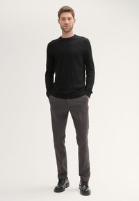 Black knit sweater, gray pants, and black shoes. The sweater has a round neck and ribbed cuffs; pants are straight-legged with a smooth texture.