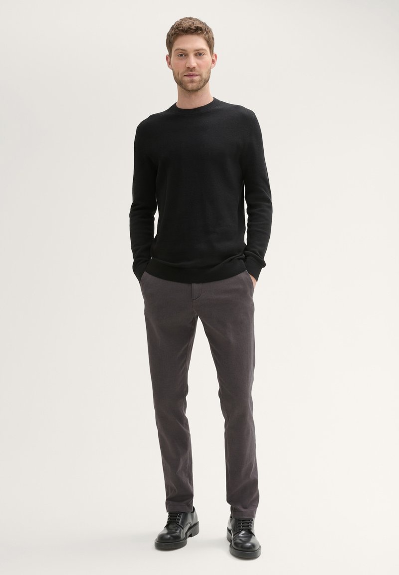 Black knit sweater, gray pants, and black shoes. The sweater has a round neck and ribbed cuffs; pants are straight-legged with a smooth texture.