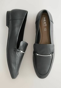 Čierne kožené mokasíny s okrúhlou špičkou, hladkou textúrou a striebornými kovovými detailmi. Dizajn zahŕňa slip-on štýl a minimálne šitie.