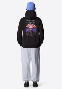 Felpa nera con una grafica sul retro caratterizzata da colori vivaci e testo. I pantaloni sportivi grigio chiaro e le scarpe nere completano l'outfit.