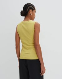 Top giallo a coste senza maniche con un design aderente. Tessuto testurizzato, scollatura rotonda e dettagli sul retro. Abbinato a pantaloni neri.