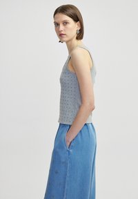 Grijze mouwloze top met textuurdetails, gecombineerd met lichtblauwe denim broek met wijde pijpen en geborduurde accenten.