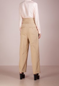 Pantalons beiges taille haute avec un design à jambes larges, dotés d'une ceinture, de poches arrière et d'une texture lisse, associés à un chemisier en satin rose clair.