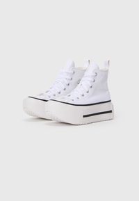 Sneakers alti bianchi in tela con occhielli metallici, lacci piatti e una soletta spessa con un dettaglio a striscia nera.