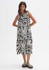 Black and white patterned sleeveless dress with a flowy silhouette. Paired with green and black sandals. Textured fabric, loose fit.