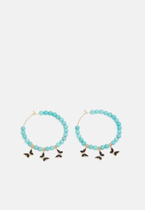 Boucles d'oreilles créoles avec perles turquoise et trois breloques papillon noires suspendues à chaque créole sur fond blanc.