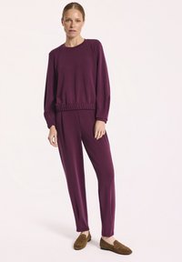 Fioletowy zestaw składający się z długiego rękawa bluzki typu crewneck z marszczonym paskiem w talii oraz dopasowanych spodni, uzupełniony brązowymi zamszowymi mokasynami.