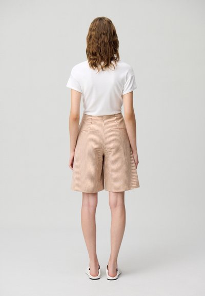 Shorts rayados en beige y naranja con una cintura alta y dos bolsillos traseros, combinados con una camiseta blanca simple y calzado ligero.