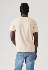 Beige bomulds t-shirt med korte ærmer, afslappet pasform og rund halsudskæring. Kombineret med lyseblå denim jeans, hvilket viser et afslappet look.