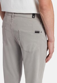Pantalons gris clair en tissu doux, dotés de poches arrière et d'une étiquette sur la taille. Le design comprend des détails de couture subtils.