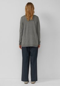 Grijze gebreide trui met lange mouwen en een iets langere achterkant. Gecombineerd met brede, donkere blauwe broek en lichte schoenen.