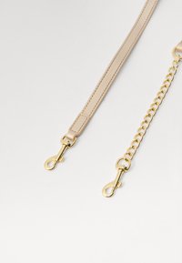 Beige leren band met goudkleurige hardware, voorzien van een dunne sectie en een kettinglinkontwerp met meerdere clips.