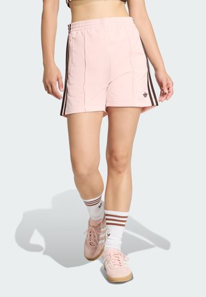 Rosa treningsshorts laget av lett stoff med svarte sidestriper. Kombinert med rosa joggesko og hvite sokker med brune striper.