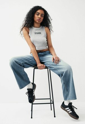 Top scurt gri cu inscripția "Melrose Avenue LOS ANGELES", asortat cu blugi largi de culoare albastru deschis și adidași negri.
