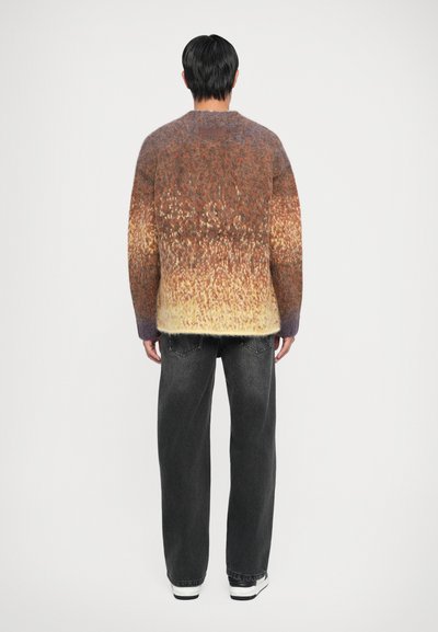 Kootud sviiter, millel on gradientvärvid pruunist kollaseni, lõdva istuvuse ja pehme tekstuuriga. Kombineeritud laiade mustade teksade ja sneaksidega.