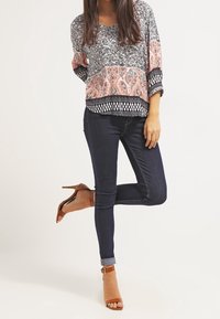 Blusa con estampado floral en tonos negro y rosa, de corte holgado, combinada con jeans de mezclilla oscuros y tacones de tiras color beige.