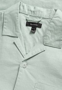 Light green linen shirt featuring a notch collar, single button closure, and small pocket. Label displays brand name and size L.