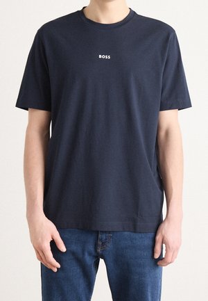Person iført en ensfarvet mørk navyblå t-shirt med korte ærmer og ordet "BOSS" trykt med små hvide bogstaver på brystet.