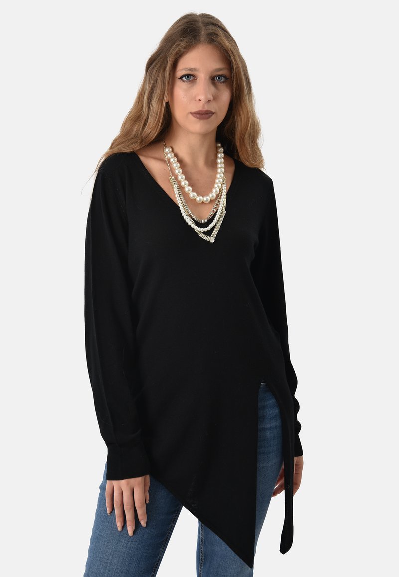 Tunic nera a maniche lunghe con scollatura a V e orlo asimmetrico. Abbinata a jeans, accentuata da collane di perle sovrapposte. Texture liscia.