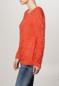 Mjuk orange tröja med långa ärmar och en lös passform; har en bred halsringning och texturerad tyg för extra dimension.