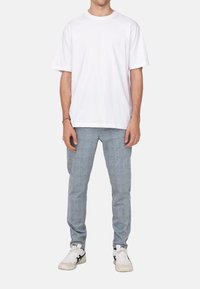 Weißes Baumwoll-T-Shirt, lockerer Schnitt, kombiniert mit hellgrauen, strukturierten Hosen mit einem dezenten Karomuster. Abgerundet mit weißen Sneakers.