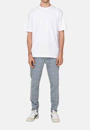 Weißes Baumwoll-T-Shirt, lockerer Schnitt, kombiniert mit hellgrauen, strukturierten Hosen mit einem dezenten Karomuster. Abgerundet mit weißen Sneakers.