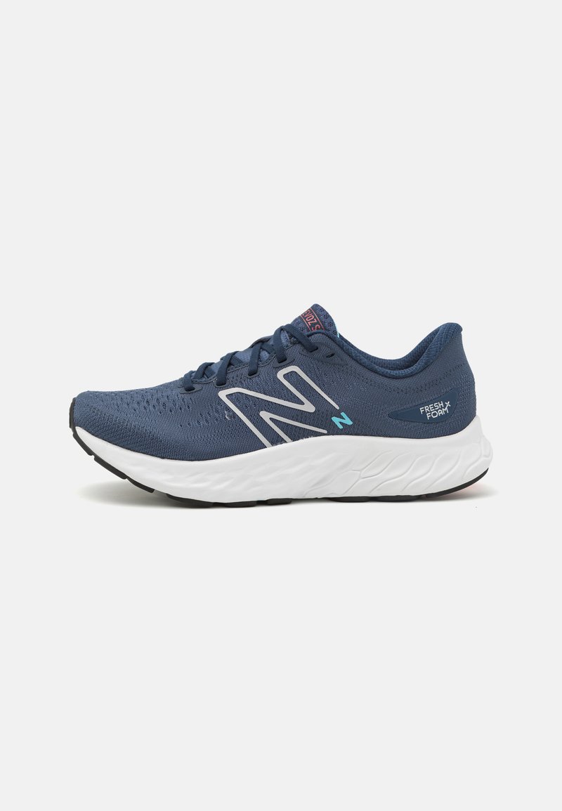 Blaue Sportschuhe mit einem atmungsaktiven Mesh-Obermaterial, weißer Zwischensohle, schwarzem Außensohle und reflektierenden Akzenten. Verfügt über ein großes "N"-Logo an der Seite.