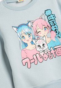 Sudadera azul clara con dos personajes de dibujos animados con orejas de gato, uno con cabello azul y el otro con cabello rosa, junto con un gráfico de un gato blanco.