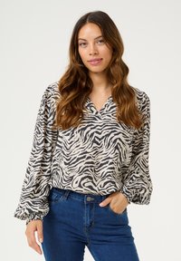 Bluse mit Zebra-Muster aus leichtem Stoff, mit V-Ausschnitt, puffärmeligen Ärmeln mit elastischen Bündchen und lockerer Passform, kombiniert mit blauen Jeans.