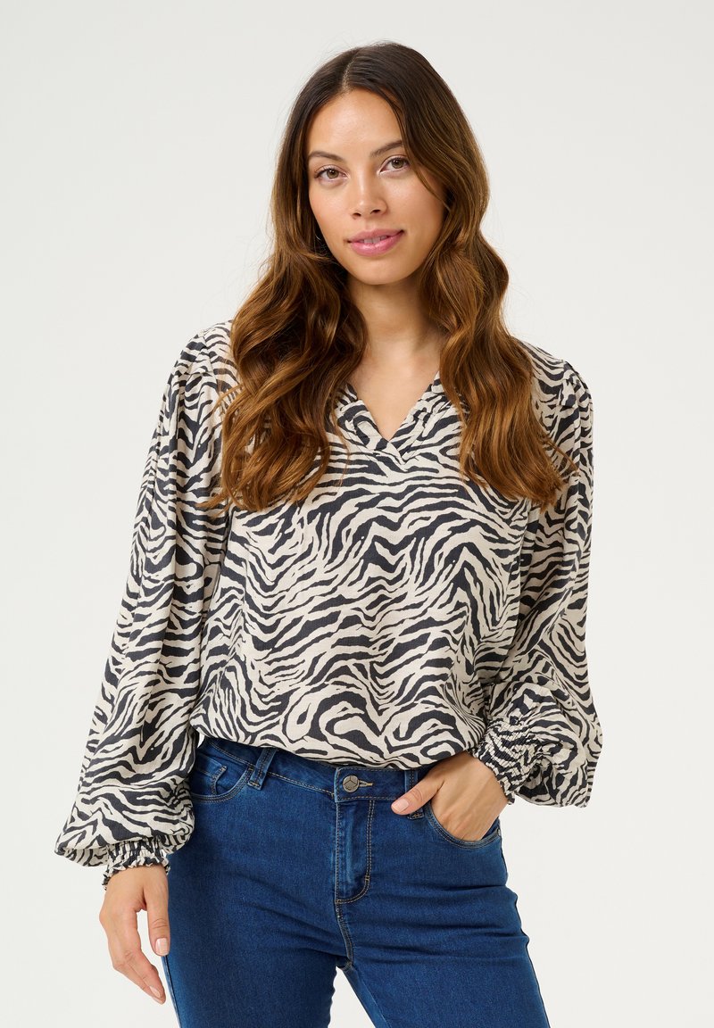 Bluse mit Zebra-Muster aus leichtem Stoff, mit V-Ausschnitt, puffärmeligen Ärmeln mit elastischen Bündchen und lockerer Passform, kombiniert mit blauen Jeans.