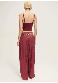 Maroon, ribbed crop top with thin straps paired with loose, crinkled maroon pants. Accented with a silver circular belt.