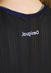 Vêtement plissé noir avec une bordure bleue scintillante au niveau du col, portant le mot "Desigual" imprimé en blanc au dos.