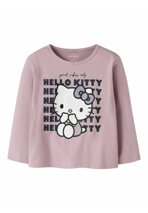 Chemise lilas à manches longues avec un motif Hello Kitty assise, avec un nœud sur la tête, et le texte "good vibes only" répété "HELLO KITTY" en noir.