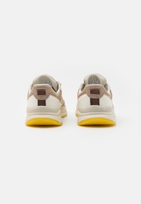 Sneaker mit braunem Wildleder-Obermaterial, beigen Lederakzenten und gelben Gummisohlen. Die Rückansicht zeigt gepolsterte Kragen und Ziehschlaufen.