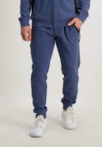 Marineblauwe sweatpants van zachte stof, met zijzakken en taps toelopende manchetten. Gecombineerd met witte sneakers voor een casual uitstraling.