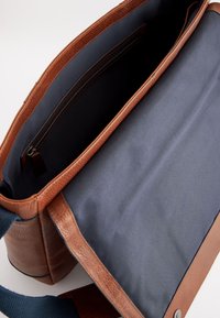 Geantă de mesager din piele maro cu suprafață texturată, având un interior din material textil închis la culoare, un buzunar cu fermoar și o curea albastră.